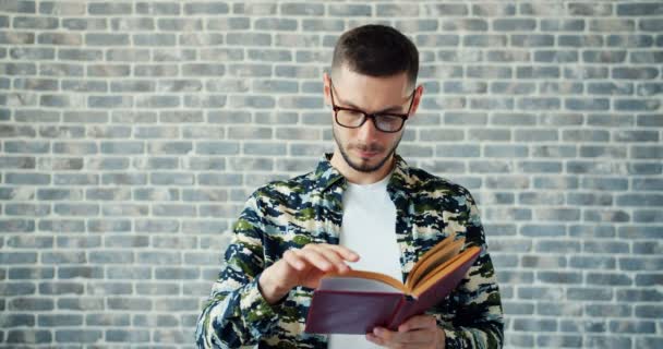 Portrait de type barbu dans des lunettes étudiant livre de lecture sur fond de mur de briques — Video