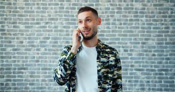 Retrato de homem alegre falando no telefone celular sorrindo no fundo da parede de tijolo — Vídeo de Stock