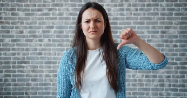 Retrato de menina infeliz mostrando polegares para baixo no fundo da parede de tijolo — Vídeo de Stock