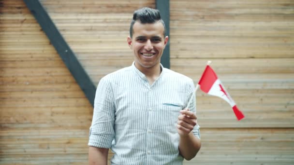 Portrait d'un homme de race mixte attrayant tenant le drapeau canadien souriant à l'extérieur — Video