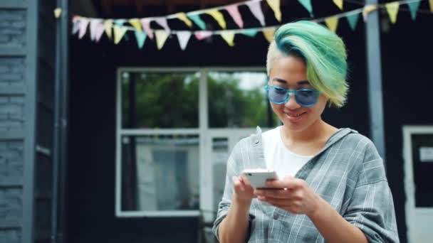 Menina asiática usando smartphone tocando tela ao ar livre desfrutando de mídia social — Vídeo de Stock