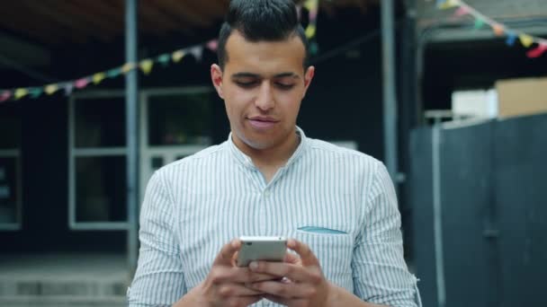 Portret van knappe gemengde race man met behulp van smartphone aanraken scherm buiten — Stockvideo