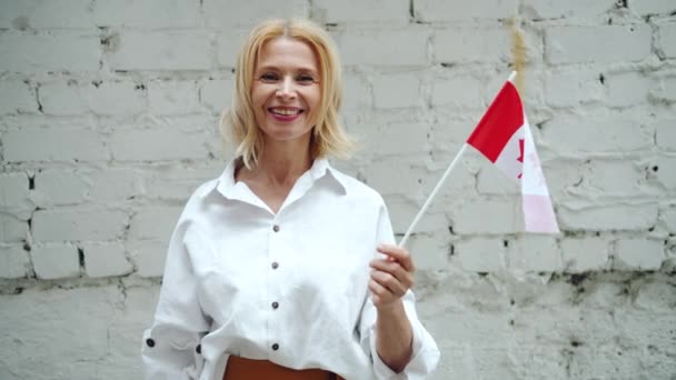 Mujer canadiense madura sosteniendo bandera nacional de Canadá sobre fondo de pared de ladrillo — Vídeos de Stock