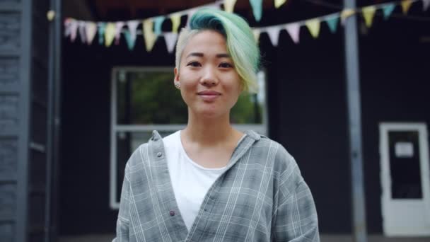 Retrato de punk asiático com nariz piercing e cabelos tingidos sorrindo ao ar livre — Vídeo de Stock