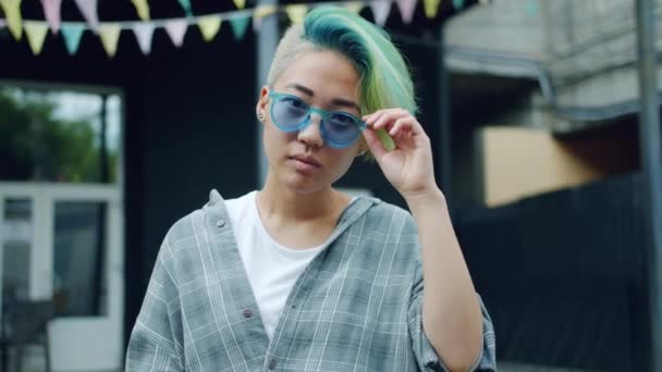 Slow Motion van vrolijke Aziatische hipster verhogen zonnebril lachend buitenshuis — Stockvideo