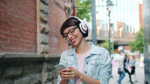 Lambat gerak gadis mendengarkan musik di headphone menggunakan smartphone outdoors — Stok Video