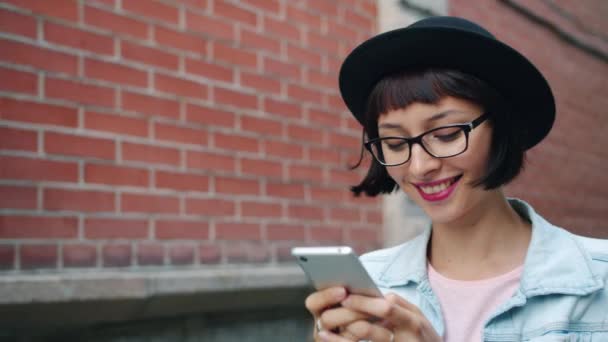 Movimento lento da menina atraente olhando para a tela do smartphone andando ao ar livre — Vídeo de Stock