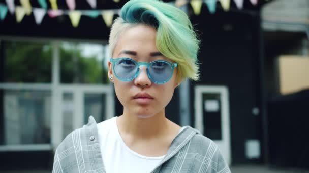 Zeitlupe eines fröhlichen asiatischen Hipsters mit Sonnenbrille, der draußen lächelt — Stockvideo