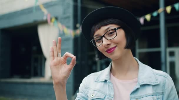 Portret van mooie jonge vrouw toont OK hand gebaar buitenshuis glimlachend — Stockvideo