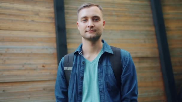 Movimento lento de homem atraente sorrindo mão acenando ao ar livre no fundo de madeira — Vídeo de Stock