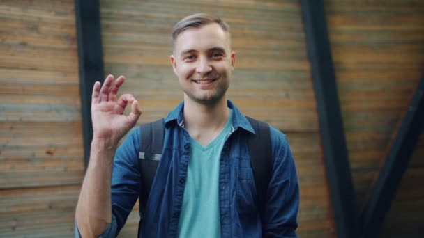 Retrato del hombre alegre mostrando el gesto OK sonriendo mirando hacia los exteriores de la cámara — Vídeos de Stock