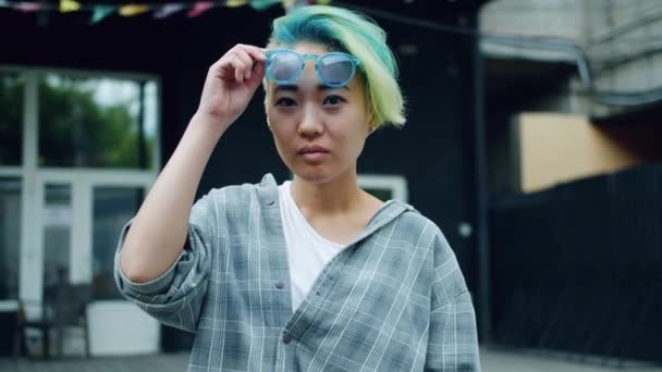 Snygg asiatisk dam tar av solglasögon och leende tittar på kamera utomhus — Stockvideo