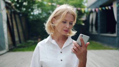 Neşeli kadın iyi haber zevk ekrana gülümseyerek bakarak akıllı telefon alıyor