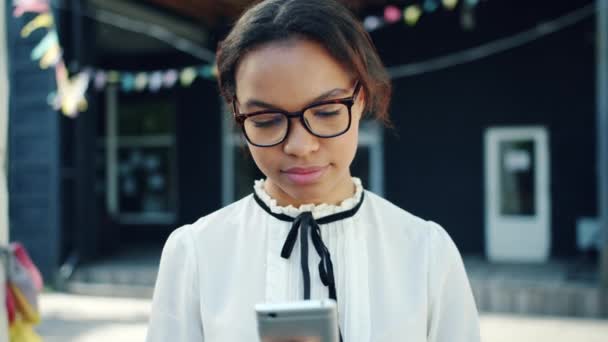 Feliz adolescente de raça mista usando smartphone moderno ao ar livre na rua — Vídeo de Stock