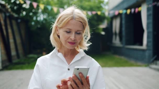 Hermosa mujer madura usando teléfono inteligente tocando la pantalla al aire libre — Vídeos de Stock