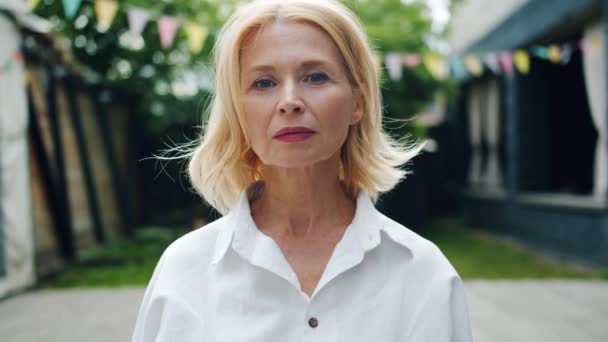 Портрет блондинки, стоящей на улице с серьезным лицом — стоковое видео