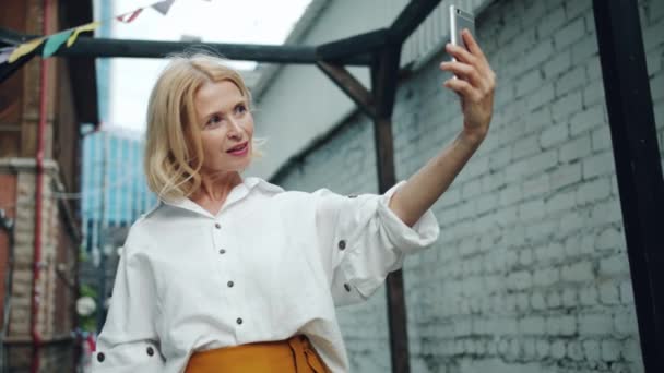 Slow motion of pretty middle aged woman taking selfie with smartphone outdoors — Stock Video