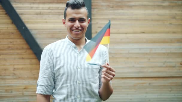 Portrait of young Arab waving German flag and smiling outdoors in city street — Stock Video