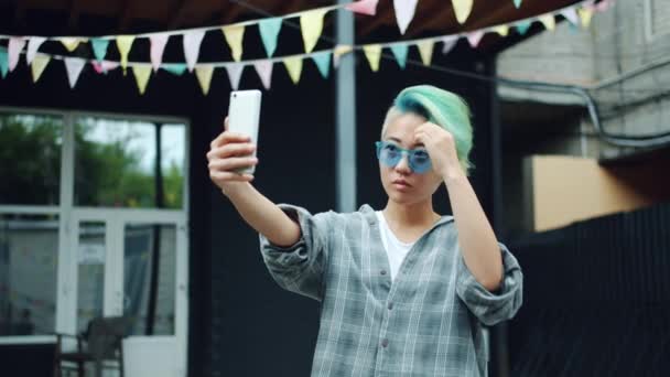 Stylish Asian girl in sunglasses taking selfie with smartphone camera outdoors — Stock Video