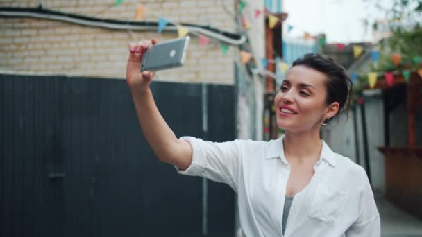 Mouvement lent de jolie dame prenant selfie à l'extérieur à l'aide d'un smartphone agitant la main — Video