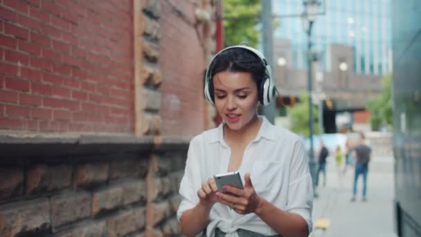 Pretty kvinna lyssnar på musik i hörlurar sjunger med smartphone utomhus — Stockvideo