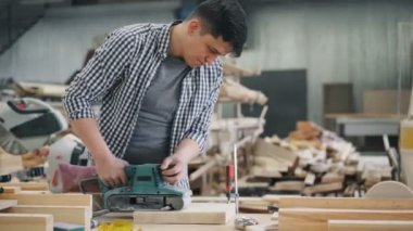 Ahşap parlatma makinesi kullanarak ahşap atölyesinde çalışan genç adam