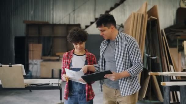 Mutlu erkek ve kadın tablet ve kağıtları tutan ahşap atölyesinde iş tartışıyor — Stok video