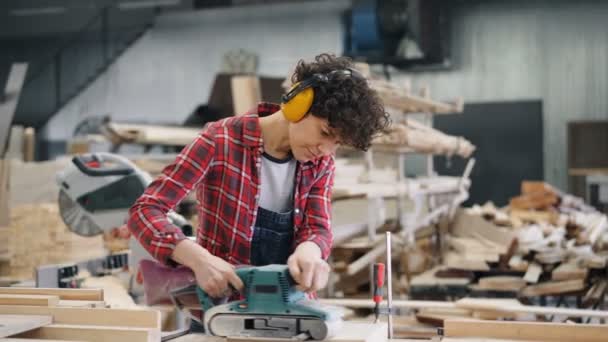 Atölyede elektrikli parlatma makinesi kullanarak ahşap ile çalışan kadın marangoz — Stok video
