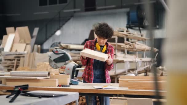 Attento falegname guardando pezzo di legno poi lucidandolo con carta vetrata — Video Stock