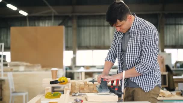 Joven carpintero trabajando con pulidora en taller en mesa de trabajo — Vídeos de Stock