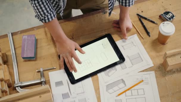 Мужские руки касаются экрана планшета с техническим рисунком мебели в мастерской — стоковое видео