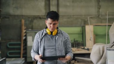 Ahşap atölyesinde yürüyen ve tablet ekranına dokunan erkek marangoz