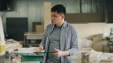Ahşap atölyesinde yürüyen tabletli genç adam kereste ve ekipmana bakıyor