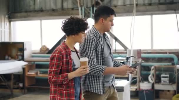 Pracownicy rozmawiają w warsztatach drewnianych, facet za pomocą tabletu, podczas gdy dziewczyna pije kawę — Wideo stockowe