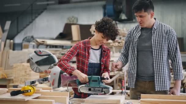 Junge Auszubildende lernen in Holzwerkstatt Umgang mit Elektropolierer — Stockvideo
