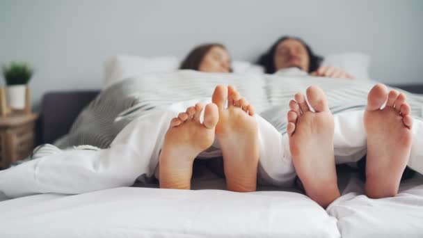 Женщина и мужчина лежат вместе в постели, спят под одеялом, сосредоточены на ногах — стоковое видео