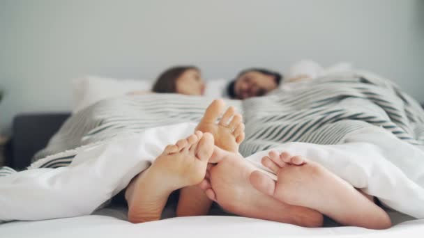 Flickor och killar fötter röra i sängen under filt medan människor som ligger tillsammans — Stockvideo