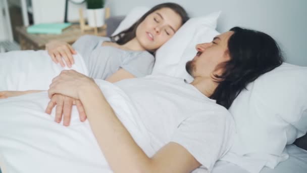 Cara irritado se escondendo sob travesseiro enquanto esposa roncando na cama durante o sono — Vídeo de Stock