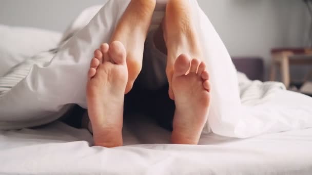 人脚有乐趣在床上毯子下，女孩发痒的家伙移动腿 — 图库视频影像