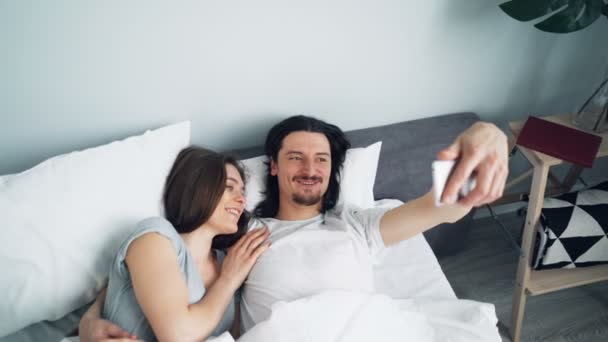 Menina e cara tomando selfie na cama com câmera do smartphone beijando abraço — Vídeo de Stock