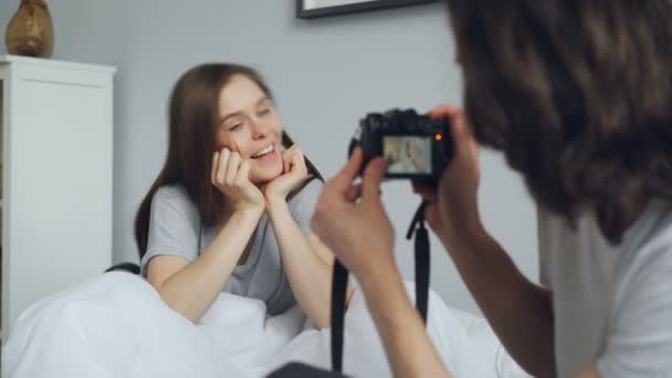 Guy figyelembe fotó örömteli lány modern kamerával ül az ágyban otthon — Stock videók