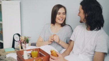 Erkek ve kadın sohbet ve evde yatakta romantik kahvaltı sırasında gülüyor