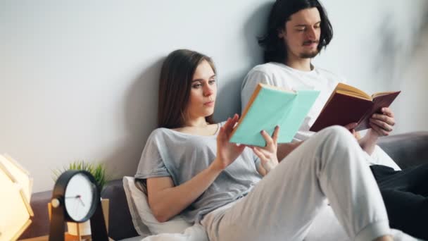 Man and woman in pajamas reading books in bed at home turning pages — Stock Video