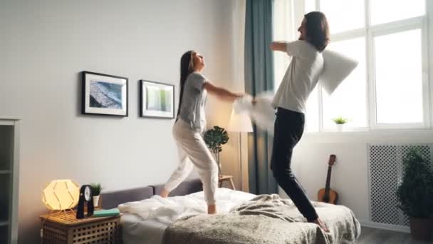 Retrato de hombre y mujer divirtiéndose con pelea de almohadas y luego besándose en la cama — Vídeo de stock