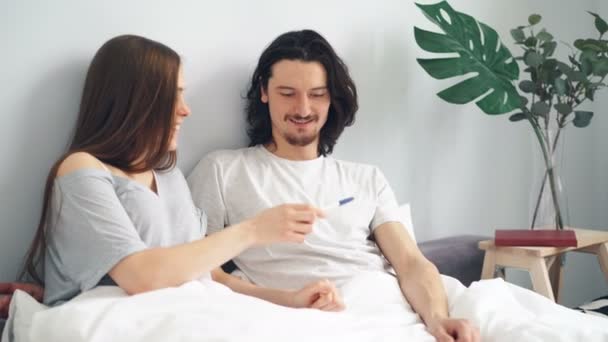 Вагітна дівчина дає хлопцеві тест на вагітність, пара цілується обіймаючись в ліжку вдома — стокове відео