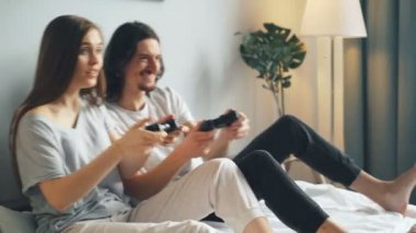 Evde yatakta video oyunu oynayan pijama lı karı koca, kazanan adam