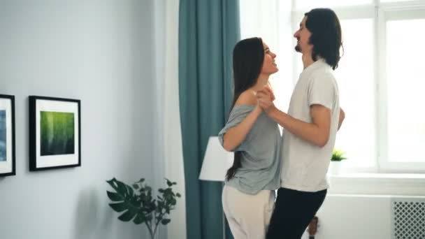 Vrolijke mensen meisje en kerel dansen op bed in flat met plezier handen vasthouden — Stockvideo