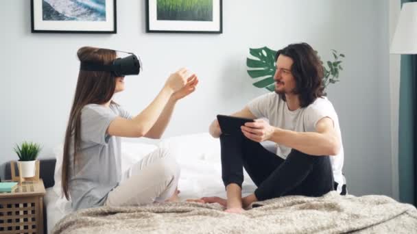 Junge Frau mit VR-Brille bewegt Hände, während Freund Tablette berührt — Stockvideo