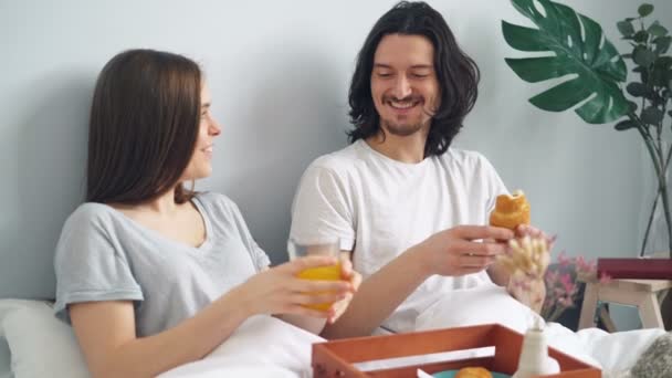 Gelukkige jonge mensen lachen chatten eten ontbijt in bed thuis — Stockvideo