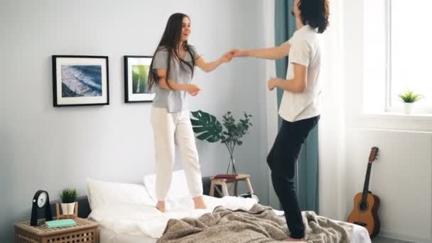 Gelukkige jonge mensen in pyjama dansen op bed thuis met plezier samen — Stockvideo